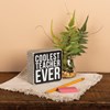 A classic black and white wooden box sign featuring a distressed "Coolest Teacher Ever" sentiment